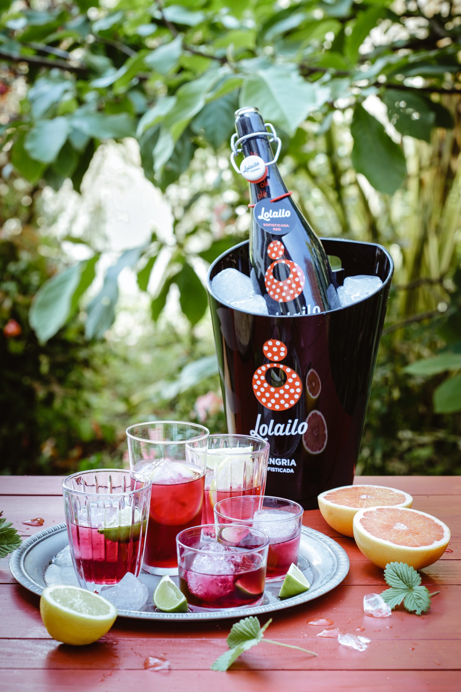 Bouteille de sangria rouge Lolailo premium présentée dans un seau à glace avec des verres garnis de fruits frais.