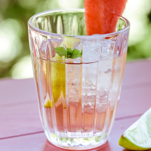 Verre de sangria rouge rafraîchissante garnie de citron, menthe et pastèque pour apéritif estival.