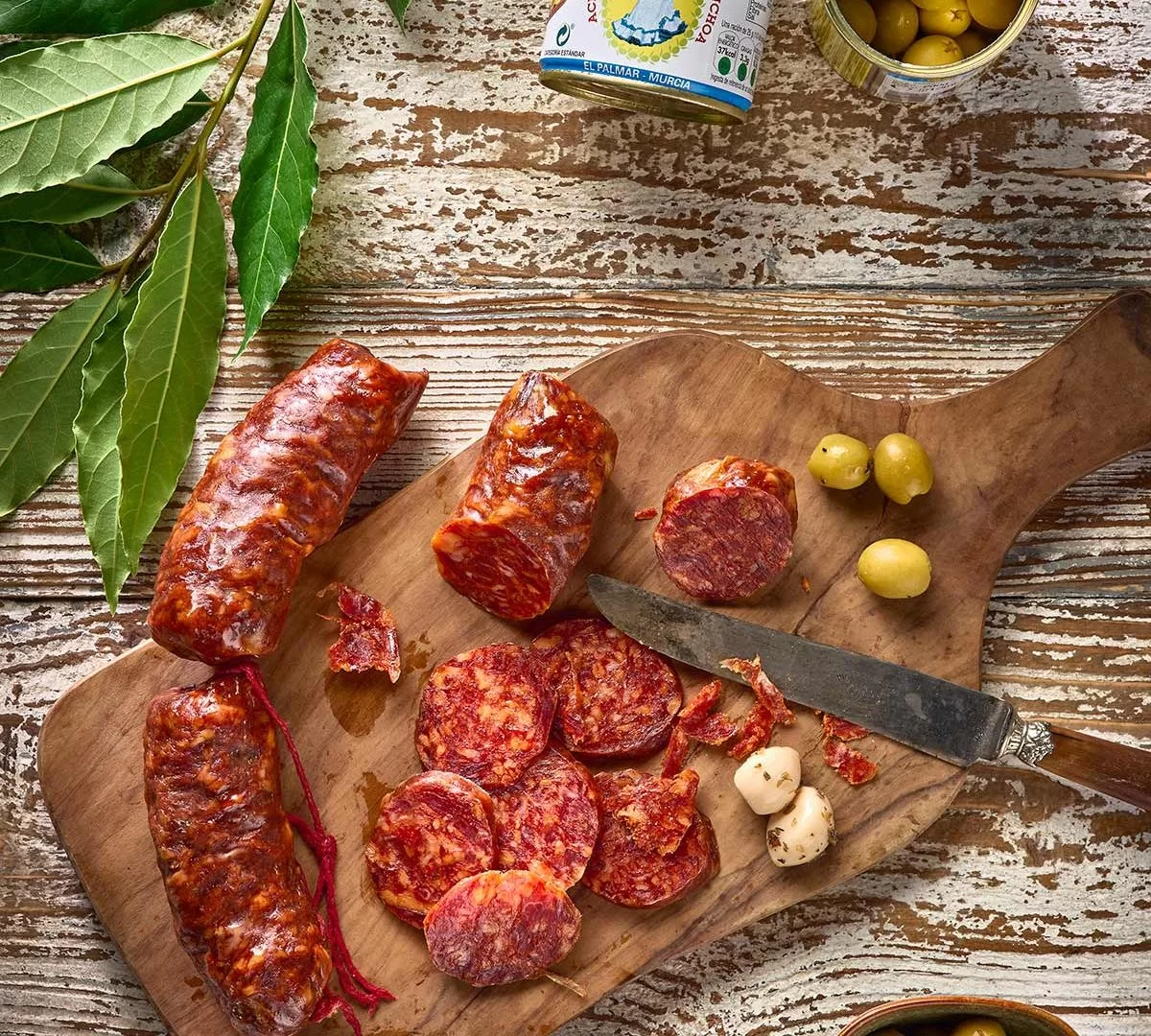 Chorizo artisanal en tranches avec olives et ail mariné sur une planche en bois rustique.