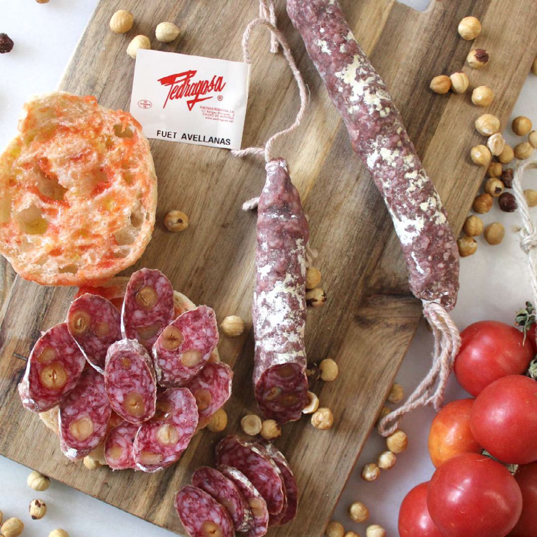 Fuet catalan aux noisettes, charcuterie artisanale sur planche en bois avec pain et tomates.