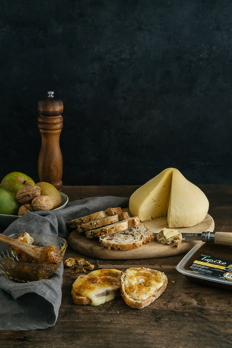 Fromage Tetilla de Galice sur une planche en bois, accompagné de pain grillé, noix et confiture.