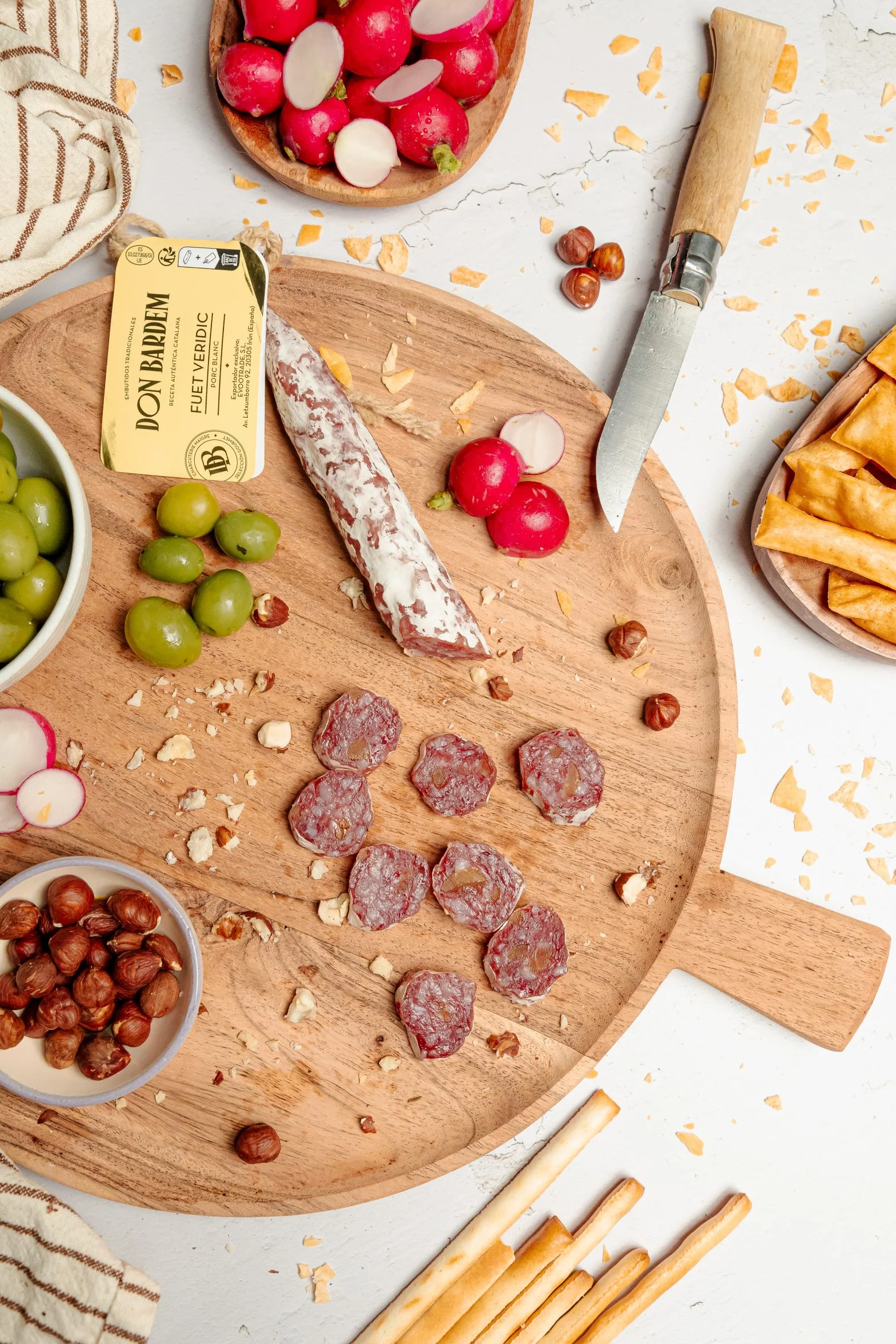 Planche de charcuterie catalane artisanale avec saucisson tranché et noisettes entières.