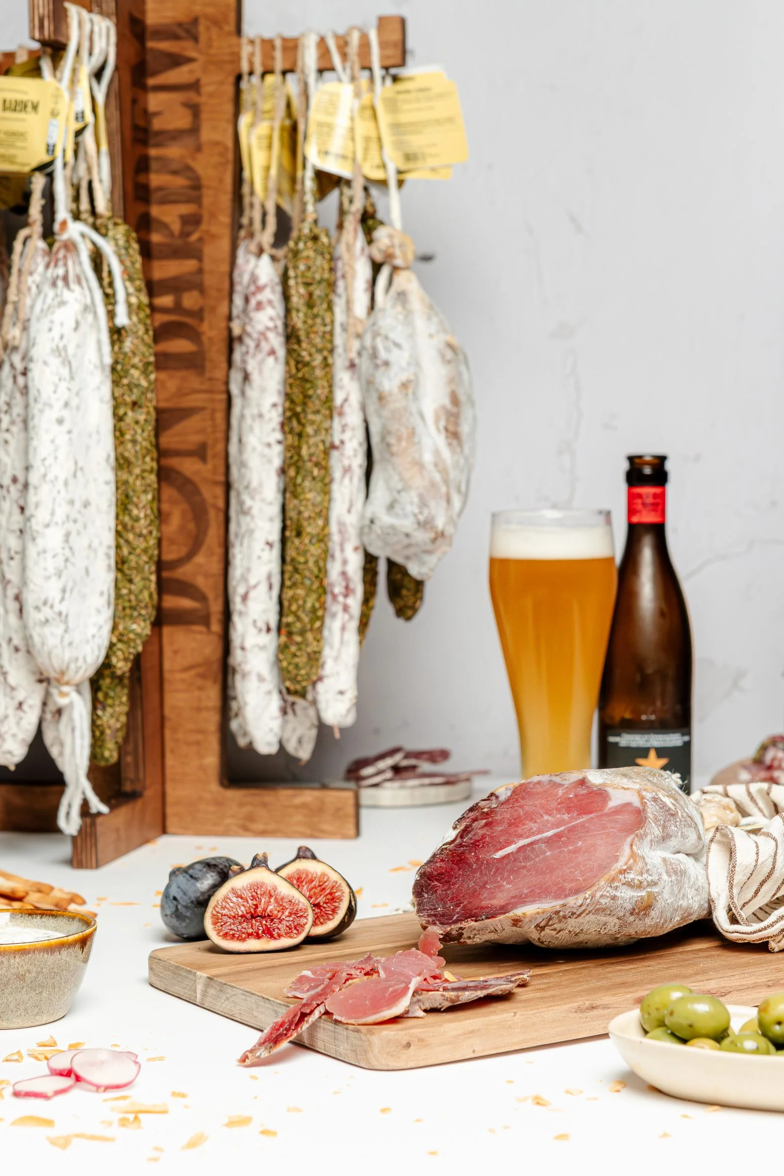 Assortiment de charcuteries catalanes artisanales accompagnées d'une bière et de figues fraîches."