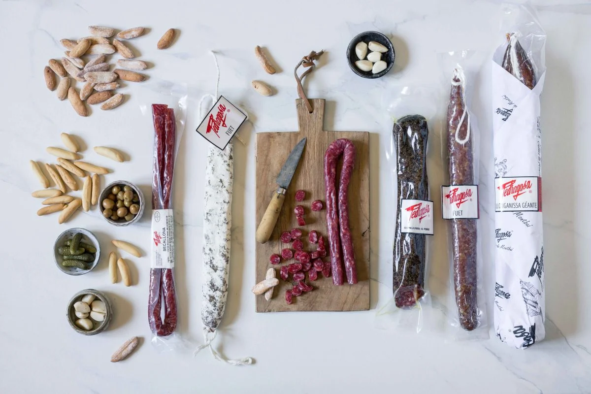 Gamme complète de charcuteries espagnoles incluant fuet, secallona et longanisse sur une planche rustique.