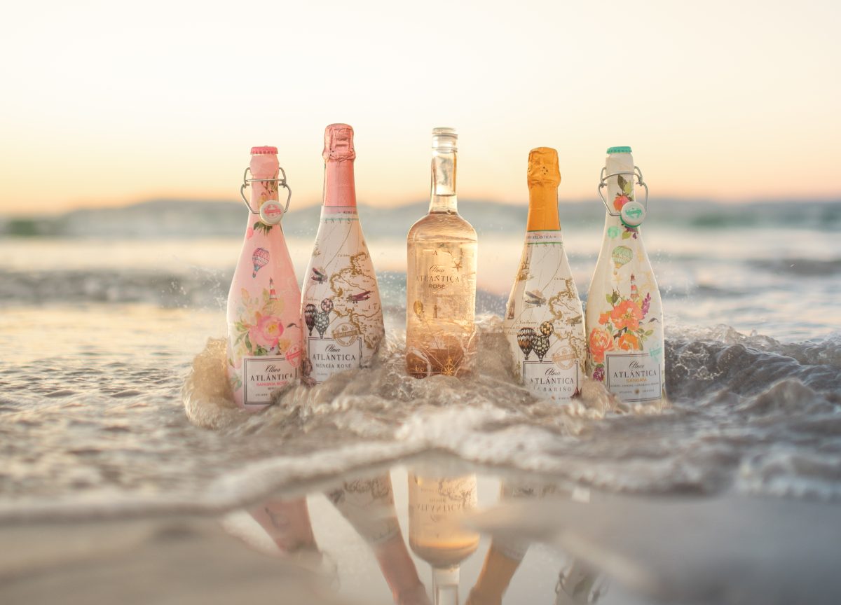 Gamme complète des vins Alma Atlántica, incluant rosé, blanc pétillant et sangria, sur une plage au coucher du soleil.