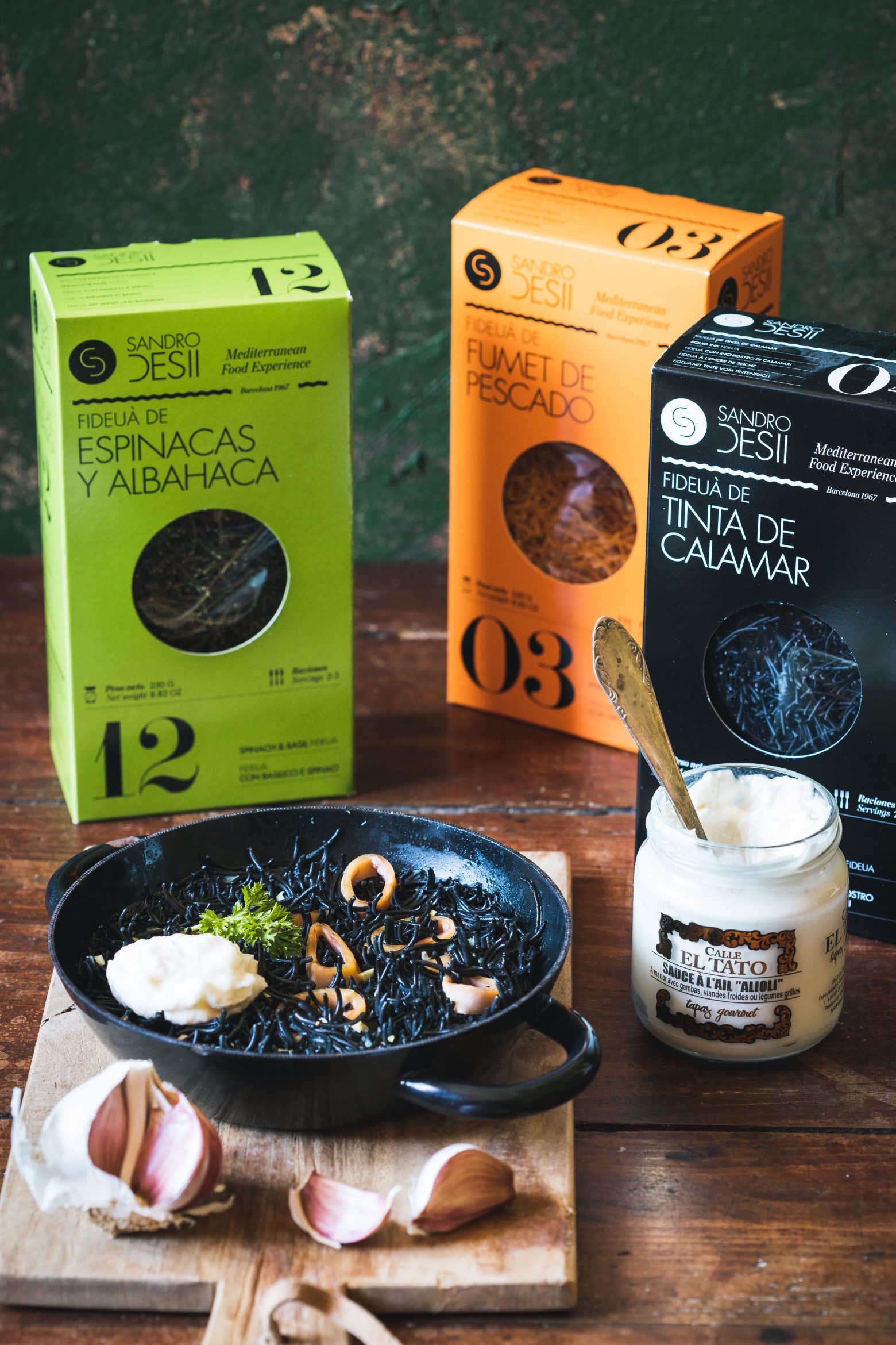 Fideuà Sandro Desii en boîtes, avec un plat cuisiné à l’encre de seiche et à l’aïoli.