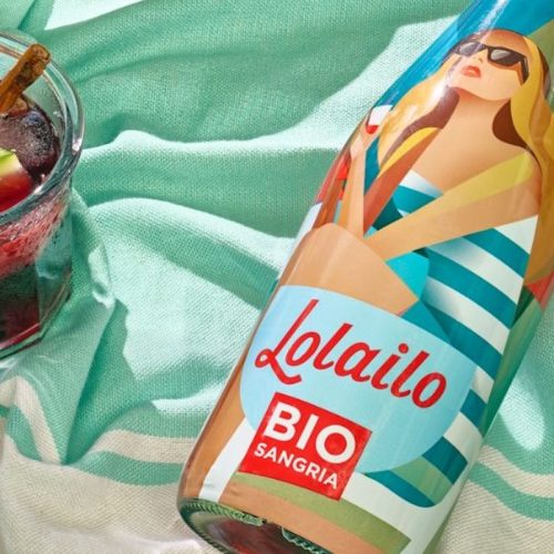 Bouteille de sangria bio Lolailo posée sur une serviette de plage avec un verre de sangria rouge