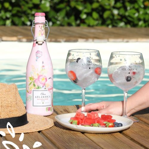Bouteille de sangria rosé Alma Atlántica et verres ballons garnis de fruits au bord d’une piscine.