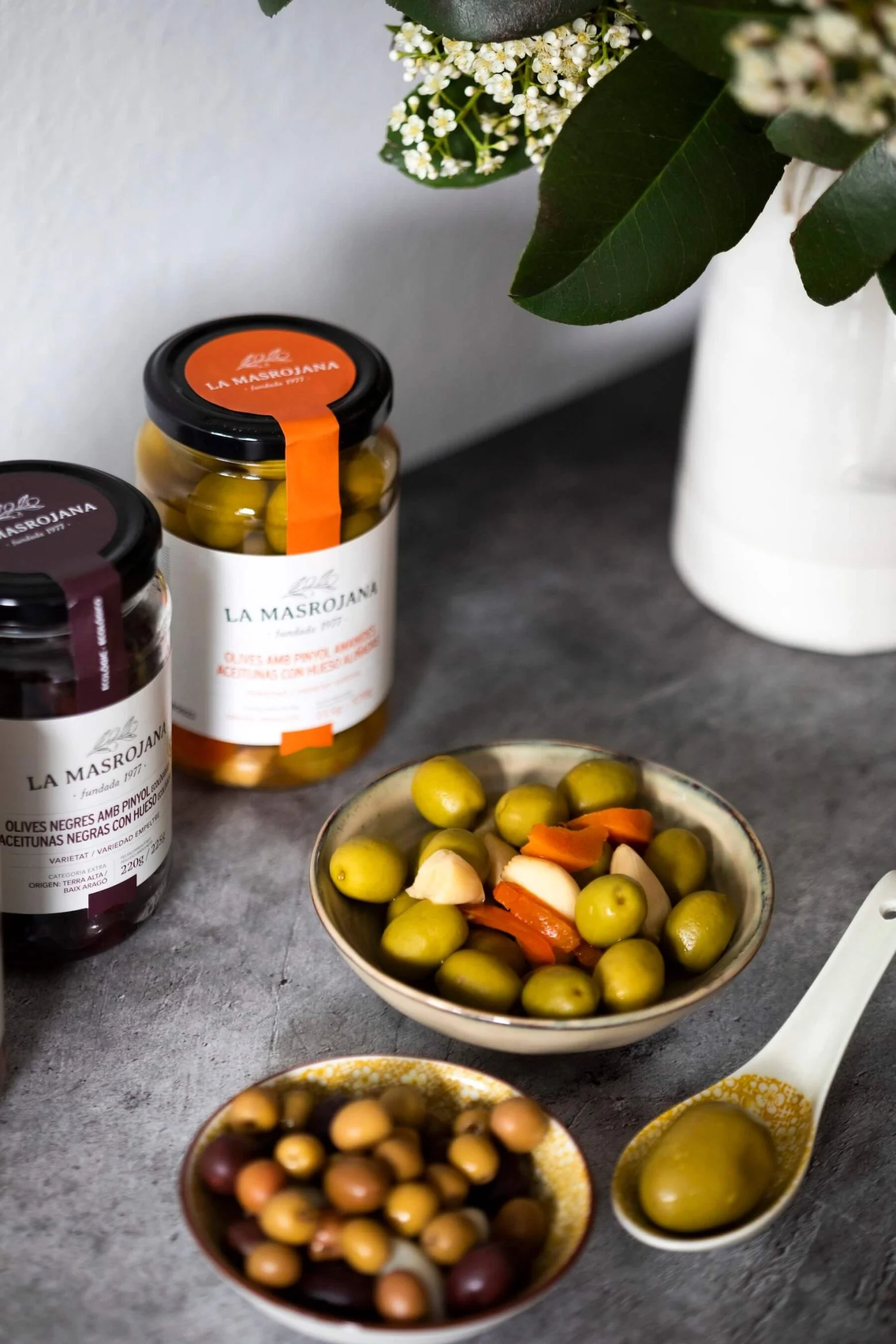 Bocaux d’olives La Masrojana et coupelles garnies d’olives vertes, noires et légumes marinés