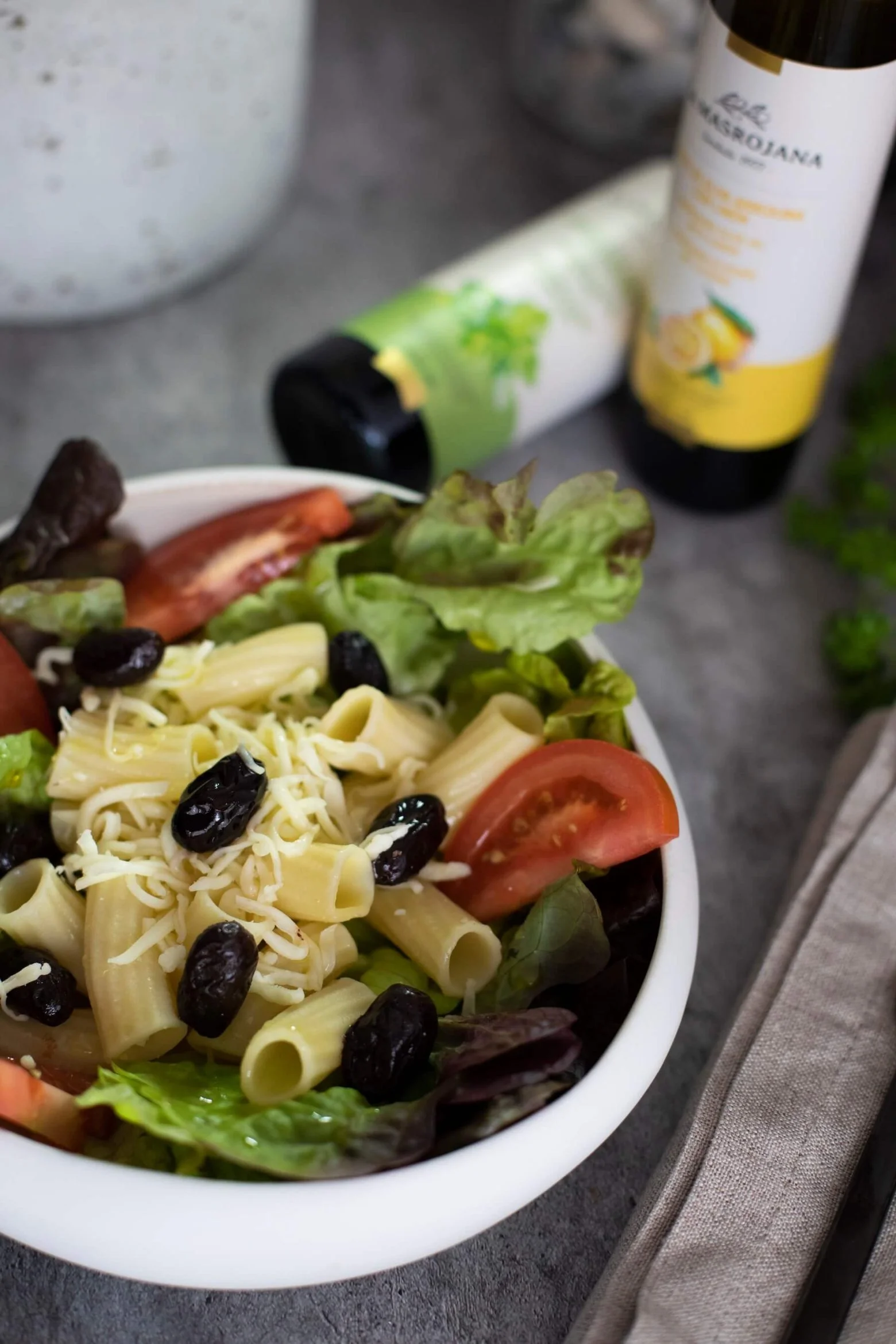 Salade de pâtes, tomates et olives avec huile La Masrojana au citron en arrière-plan