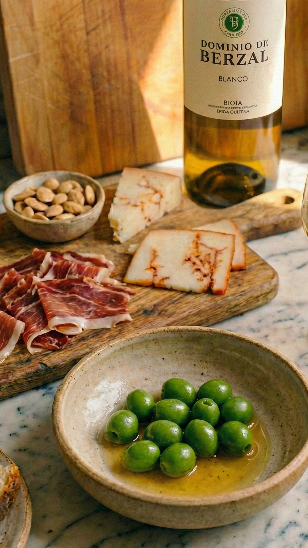 Olives vertes dans un bol, accompagnées de fromage, jambon ibérique, amandes et vin blanc.