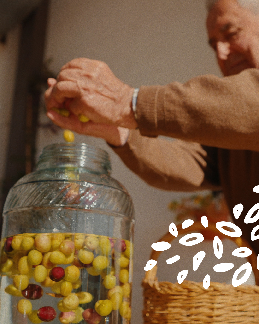 Homme âgé plongeant des olives dans un bocal de saumure, en extérieur.