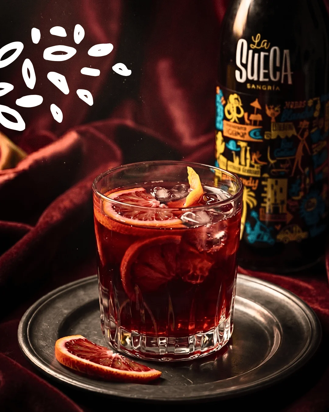 Verre de sangria La Sueca servi sur glace avec tranche d'orange sanguine et bouteille en arrière-plan.