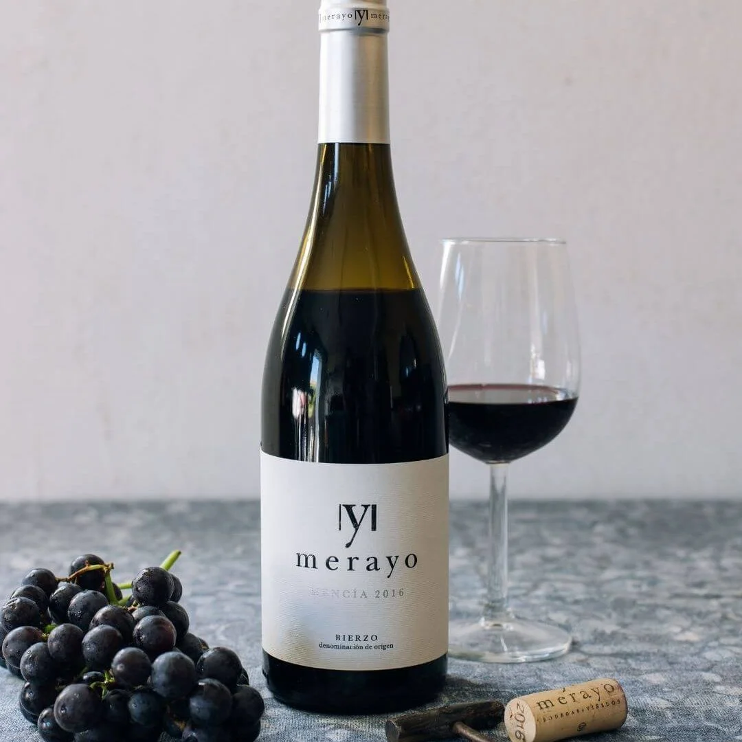 Bouteille de vin rouge Mencía Bodegas Merayo, AOP Bierzo, servie dans un verre à vin, avec une grappe de raisin noir et un tire-bouchon sur une nappe à motifs