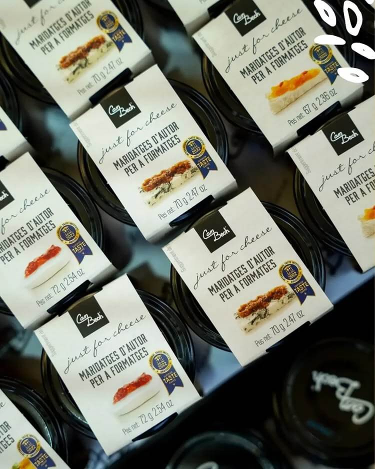 Vue rapprochée de plusieurs boîtes empilées de la gamme Just for Cheese de Can Bech, portant la mention catalane "maridatges d'autor per a formatges" et un sceau de distinction visible sur chaque emballage.