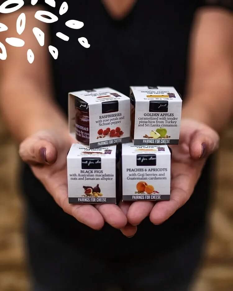 Une personne présente dans ses mains quatre boîtes de la gamme Just for Cheese de Can Bech : Raspberries, Golden Apples, Black Figs et Peaches & Apricots. Légende : Quatre parfums parmi les cinq de la gamme Just for Cheese.