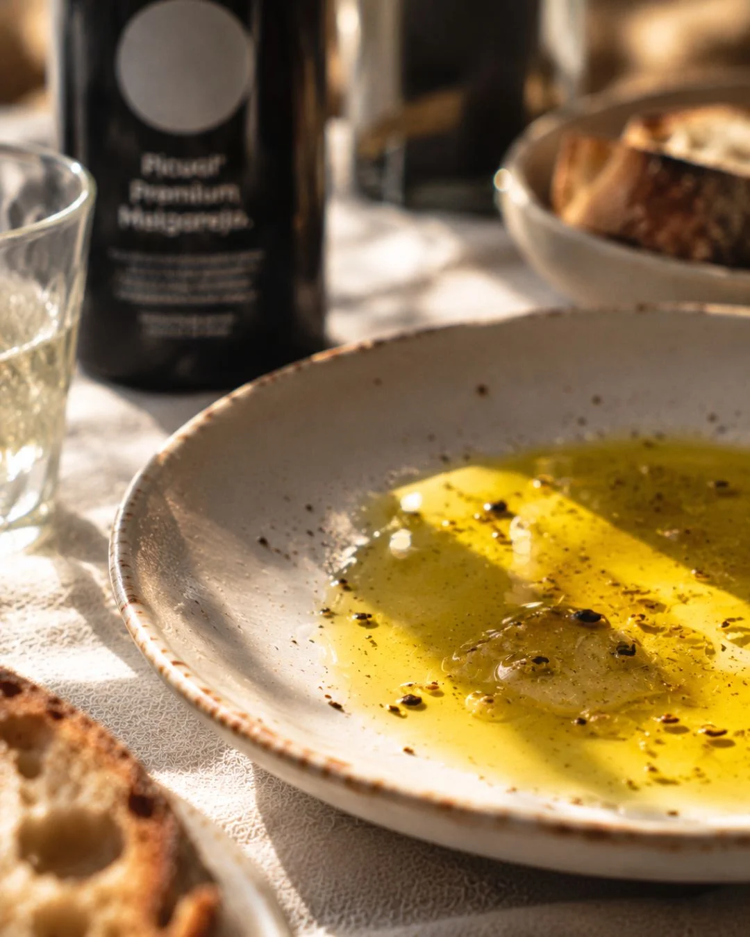 Assiette en céramique remplie d'huile d'olive vierge extra Picual Melgarejo poivrée, avec pain et bouteille en arrière-plan