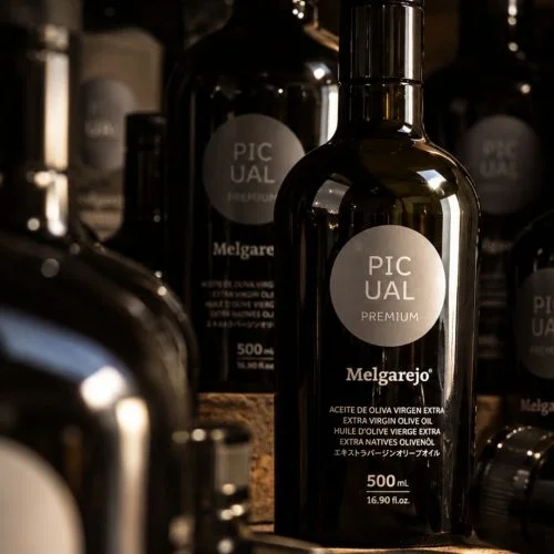 Bouteille en verre sombre de 500 ml d'huile d'olive vierge extra Melgarejo Picual Premium, entourée d'autres bouteilles