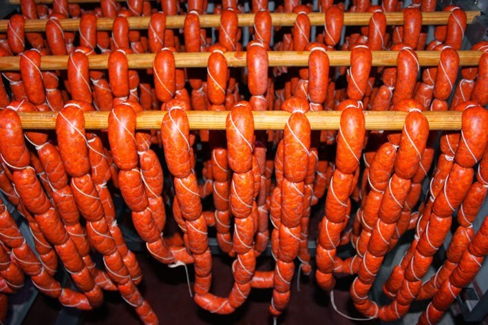 Chorizos en U ficelés, suspendus à des perches en bois dans une salle de séchage