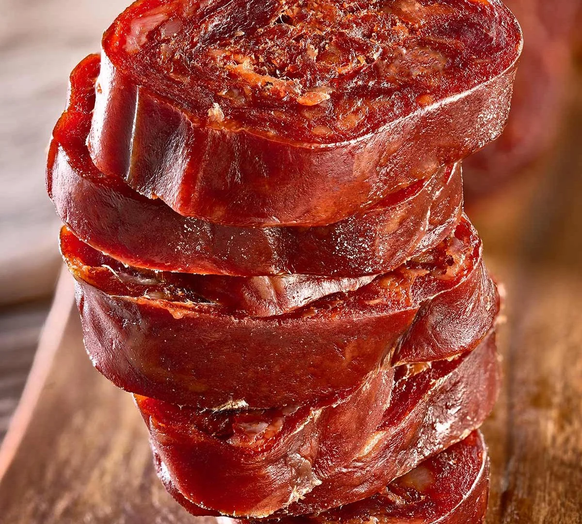 Pile de rondelles de chorizo à la coupe nette, chair rouge foncé au grain serré, sur une planche en bois