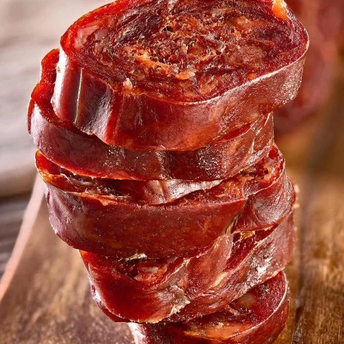 Pile de rondelles de chorizo à la coupe nette, chair rouge foncé au grain serré, sur une planche en bois